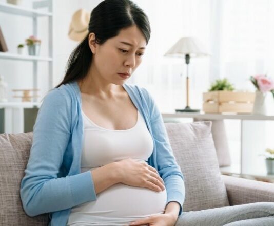 woman looking down at her pregnant belly suffering from perinatal depression