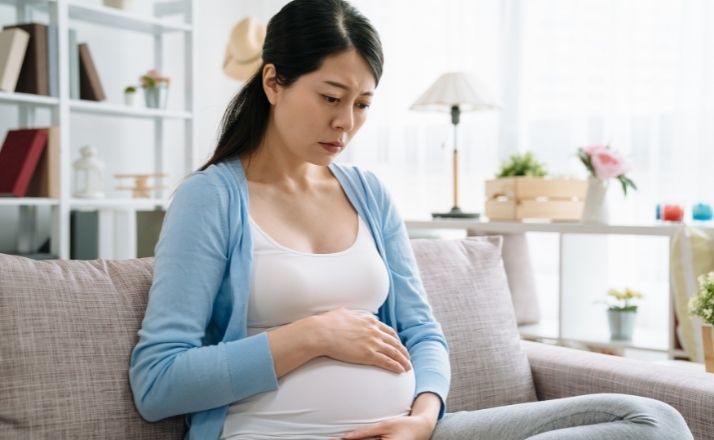 woman looking down at her pregnant belly suffering from perinatal depression