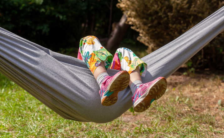 Anonymous child, school age girl laying on a hammock feet legs up, face obscured, outdoors scene, summer fun and leisure, resting, boredom abstract concept, shoes closeup, vacation, holidays