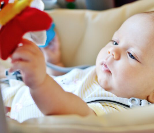 baby laying in bouncer chair and playing toy