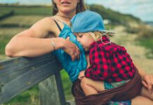 A young mother is breatfeeding her big toddler on a bench by the sea