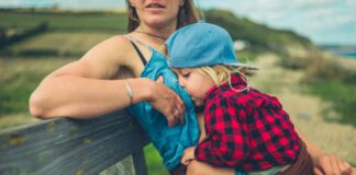 A young mother is breatfeeding her big toddler on a bench by the sea