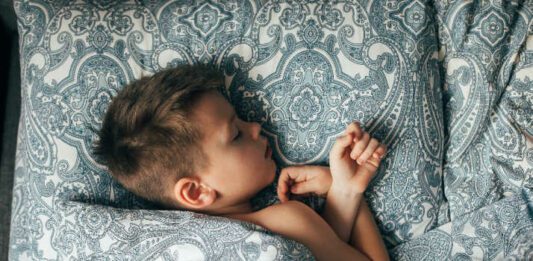 Cute boy sleeping in bed. Child 6-7 years old smiling, having a good dreams