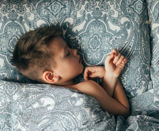 Cute boy sleeping in bed. Child 6-7 years old smiling, having a good dreams