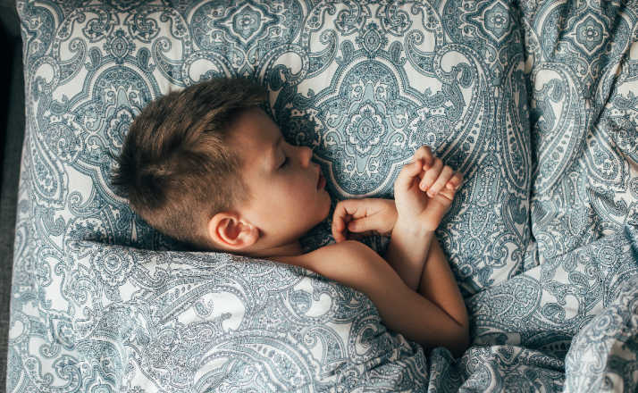 Cute boy sleeping in bed. Child 6-7 years old smiling, having a good dreams