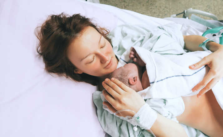 Mother holding her newborn baby child after labor in a hospital. Mother giving birth to a baby via VBAC. Parent and infant first moments of bonding.