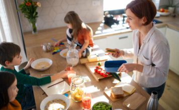 A mother of three little children packing school lunches in the kitchen at home.