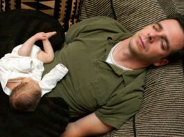 A newborn baby is curled up asleep on her sleeping father.