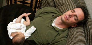 A newborn baby is curled up asleep on her sleeping father.