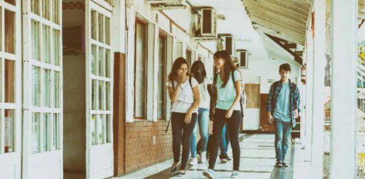 Group of mixed races teenagers group walking and smiling along school hallway.