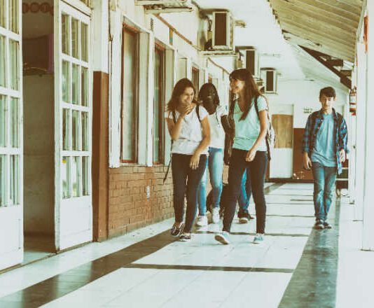 Group of mixed races teenagers group walking and smiling along school hallway.