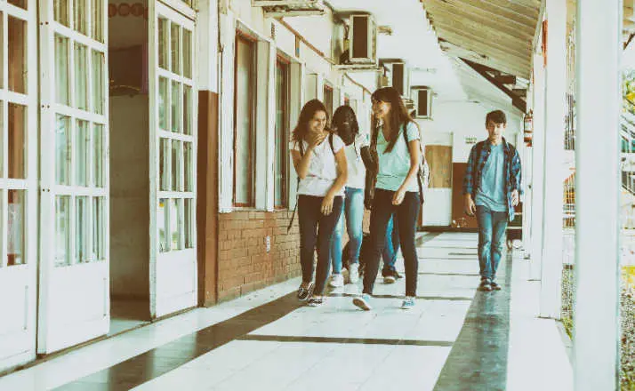 Group of mixed races teenagers group walking and smiling along school hallway.