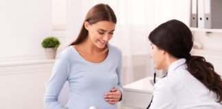 Doctor Examining Pregnant Woman Holding Stethoscope Near Belly Listening Baby's Heartbeat In Office. Pregnancy Checkup